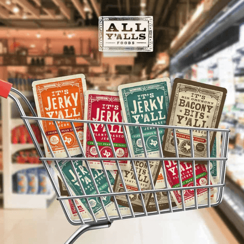 A shopping cart filled with a variety of All Y'alls Foods vegan snack sampler packs, featuring different flavors of plant-based jerky and bacon bits, on display in a grocery store aisle.