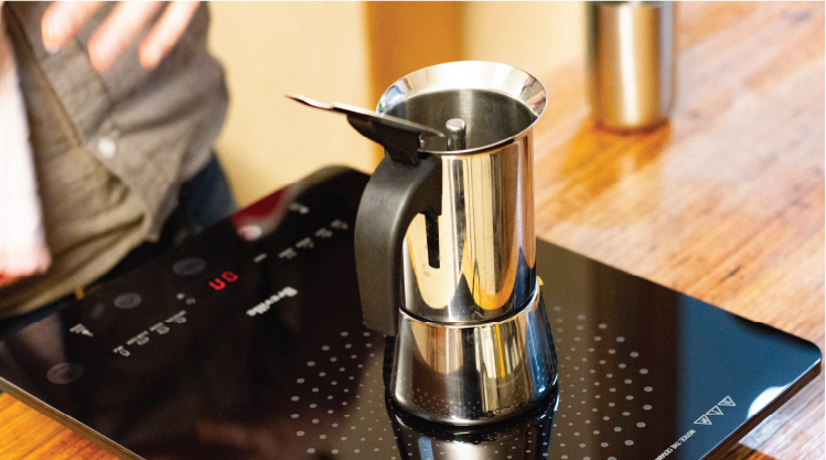 Open moka pot, sitting on portable stovetop unit. Other coffee making tools in background.