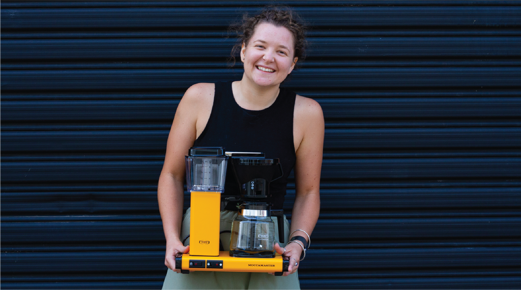 Carly from Rumble Coffee holding a Yellow Moccamaster Classic outside the Rumble Coffee Roastery in Kensington