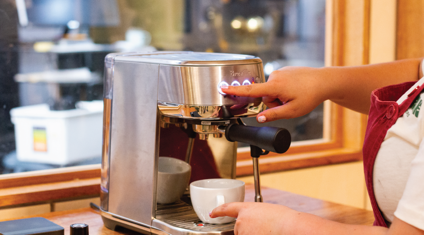 zoomed out image of breville bambino plus sitting on bench at Rumble Coffee with coffee roastery in background