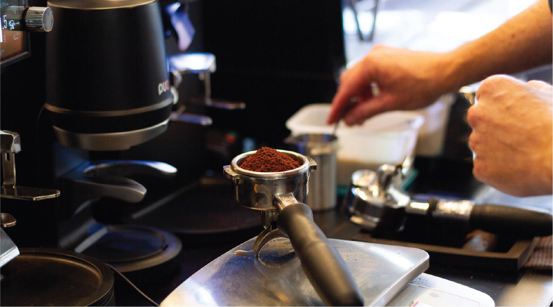 ground coffee in portafilter basket on set of scales behind a coffee machine