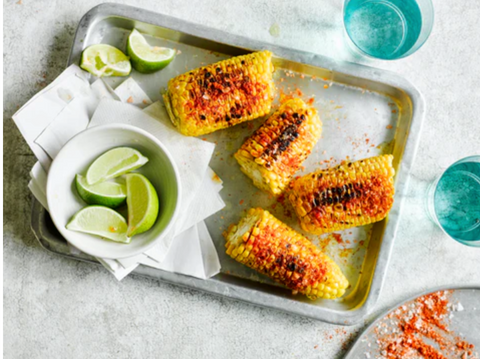 Spiced corn on the cob served on a baking tray with wedges of lime in a bowl