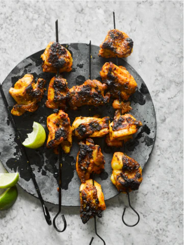 Chargrilled chicken on kebab skewers placed on a black plate with wedges of lime to serve