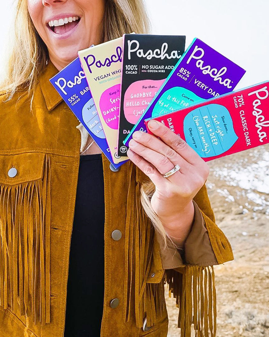 Woman with a buckskin fringe holding a collection of Pascha Organic Dark Chocolate Bars