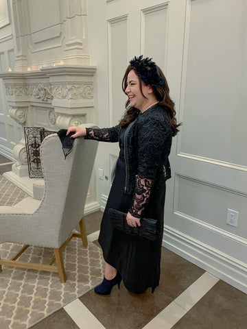 woman wearing fascinator, lace jacket, hi lo dress and booties standing in formal living room