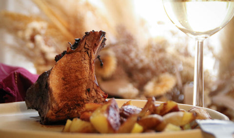 Carré de côtes de sanglier caramélisé avec des pommes de terre sautées et un verre de vin blanc.