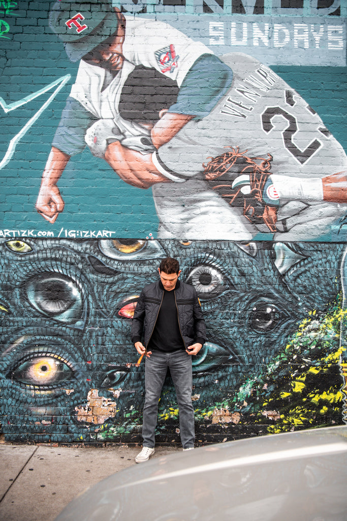 Warstic co-owner Ian Kinsler wearing the Warstic x Billy Reid Icon Player's Jacket, standing in front of a mural on Nolan Ryan putting Robin Ventura in his place. 
