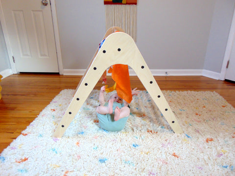 Infant playing under a Climbing triangle with scarves