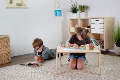 Child sitting on the floor at a lap table and child reading a book on the floor