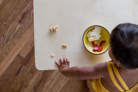 An above view shot of a boy with a child's table with a bowl of strawberries and yogurt on it 