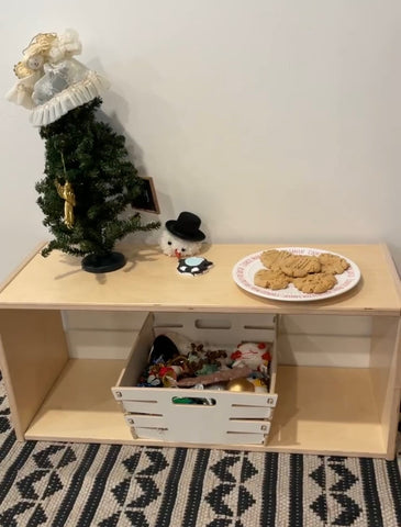 A tiny christmas tree sits on a montessori infant shelf