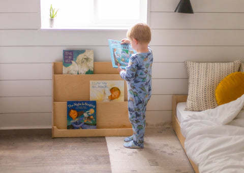 A young boy in pajamas grabbing a book off a book display shelf in his bedroom