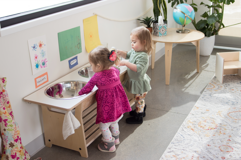 Two children standing at a washing station in a Montessori classroom