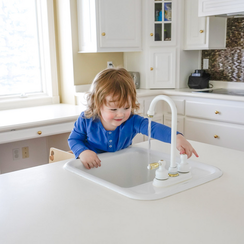A child turns on the kitchen sink standing in a Toddler Tower