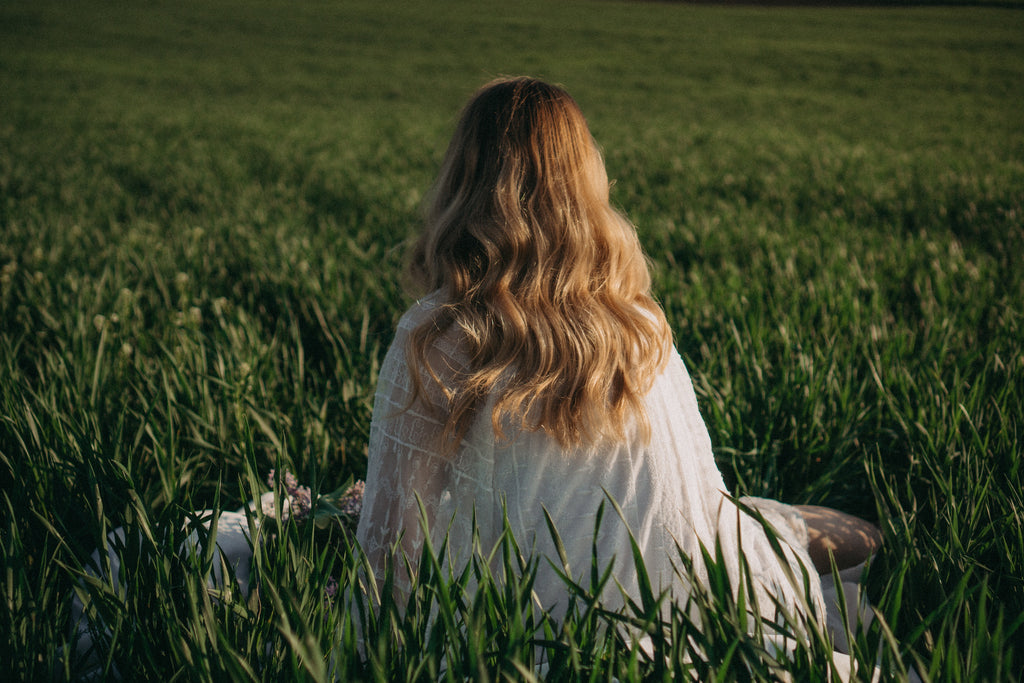 Image of woman sitting in grass field with long beautiful hair in a loose waves/curls hairstyle