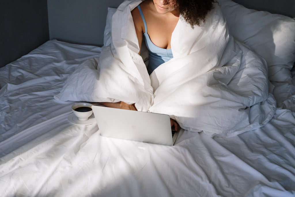 Image of woman cosy in bed with her laptop and blankets