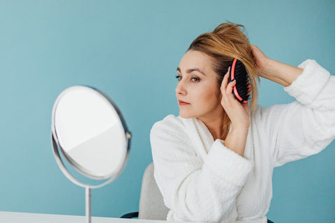 Picture of woman brushing hair in front of mirror with paddle brush