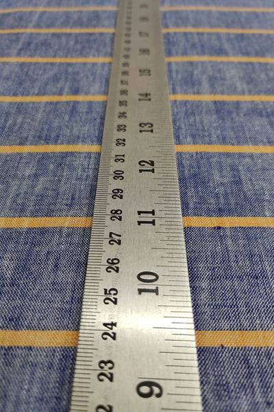 A perspective  shot of a steel measuring scale lying blue cotton khadi fabric with orange stripes.