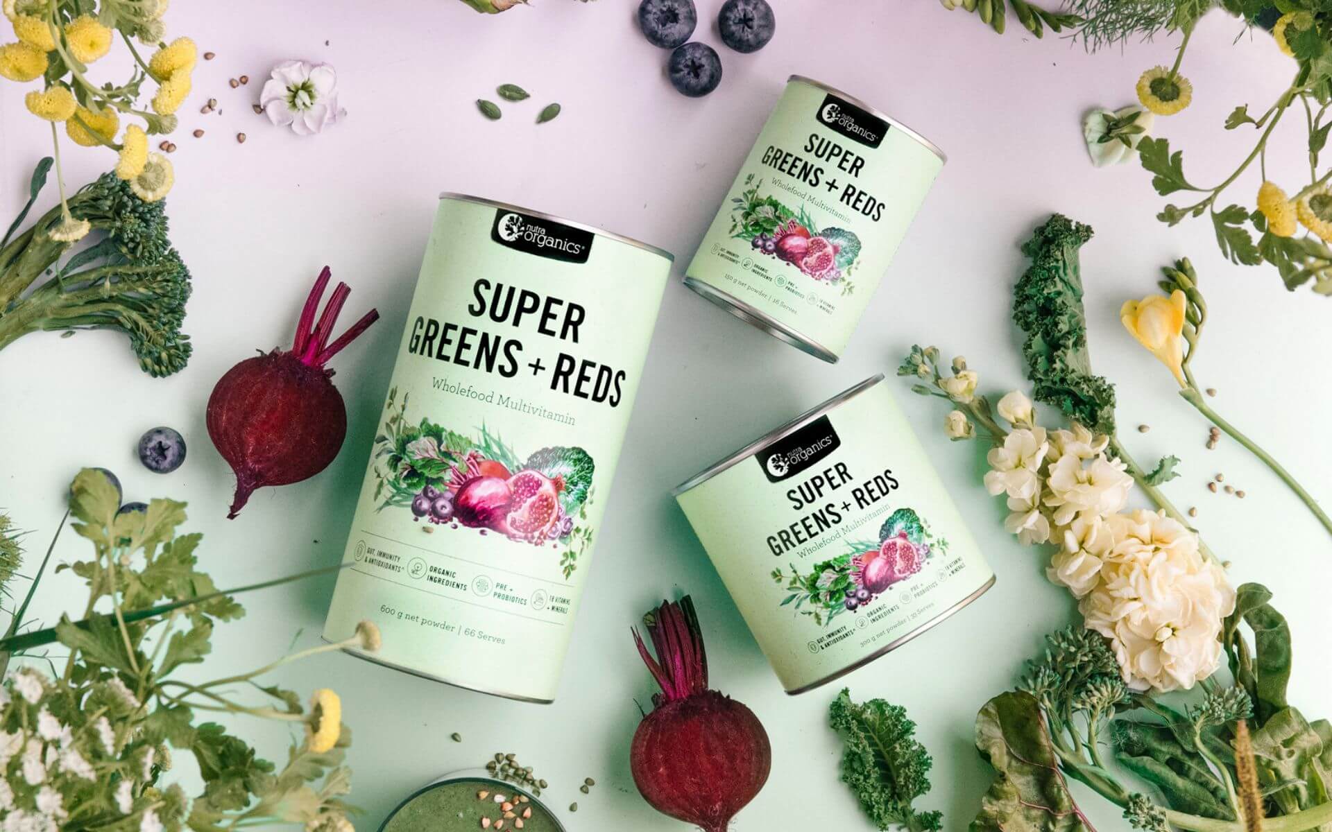 Super Greens + Reds packaging surrounded by leafy greens and beetroot