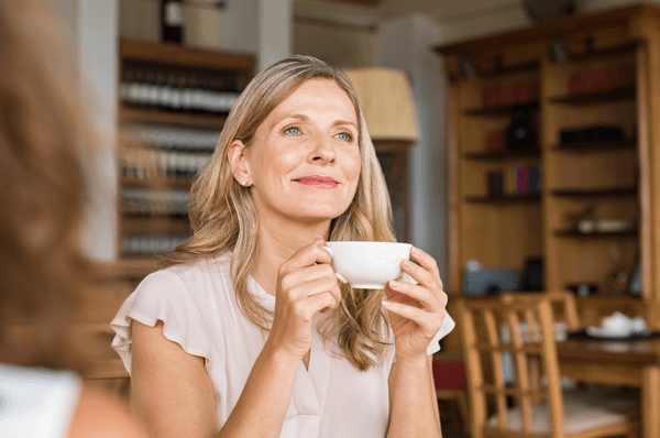 vrouw drinkt uit een kopje en kijkt tevreden naar buiten