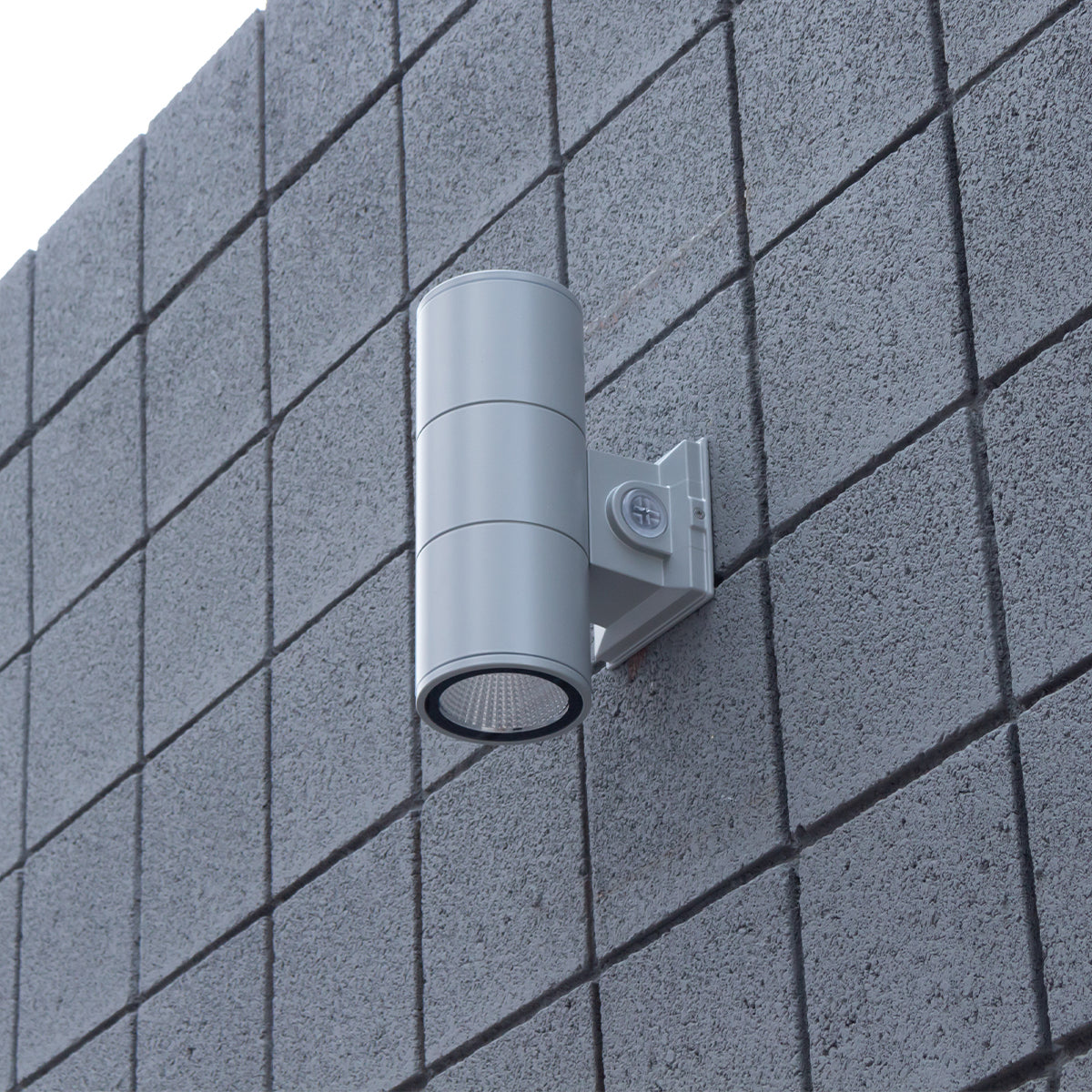 Silver up/down LED cylinder wall light mounted to a block exterior wall in daylight