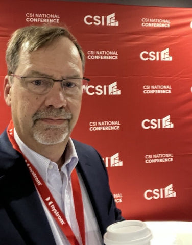 A photo of Andrew Miller posing in front of the CSI Conference event backdrop.