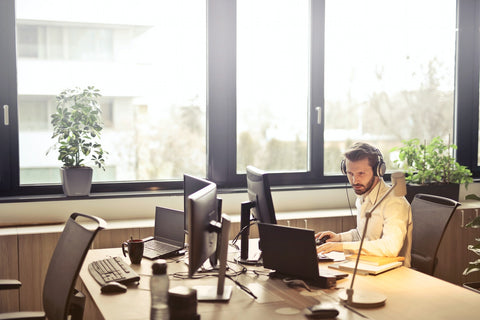 man with headphones facing laptop by big windows