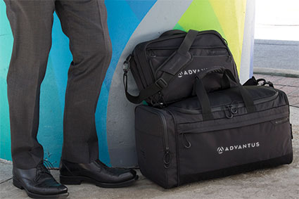 man standing next to a duffel bag and messenger bag with advantus embroidered on the side