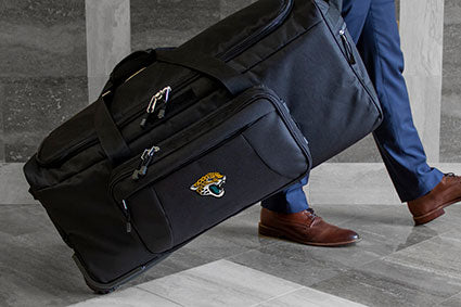 person walking with a wheeled duffel bag, embroidered nfl logo on the side