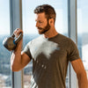 Male athlete curling a kettlebell weight in front of bright windows