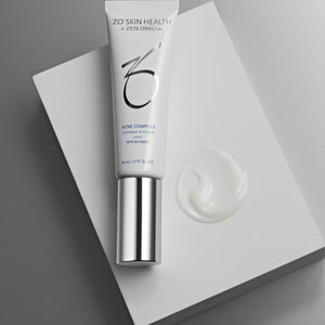 Product image of ZO® Acne Complex in sleek silver and white packaging, formulated to target all stages of acne formation, reduce active breakouts, prevent future blemishes, and improve the appearance of post-acne marks and texture