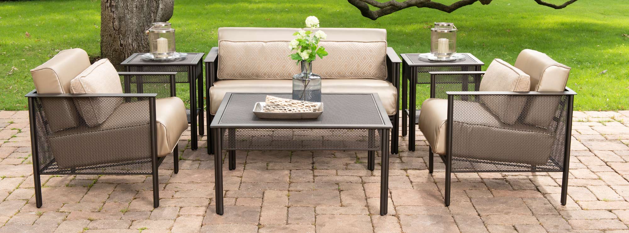 wrought iron mesh outdoor sofa set sitting under a tree on a brick patio