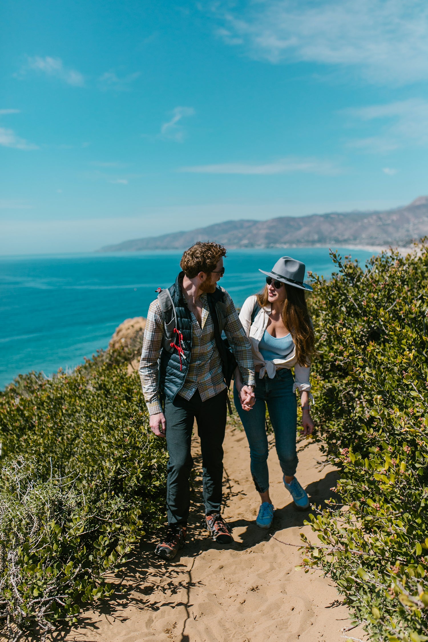 Go for a bushwalk or a hike for a great date idea. Two people hiking next to the ocean with green bushes and great view