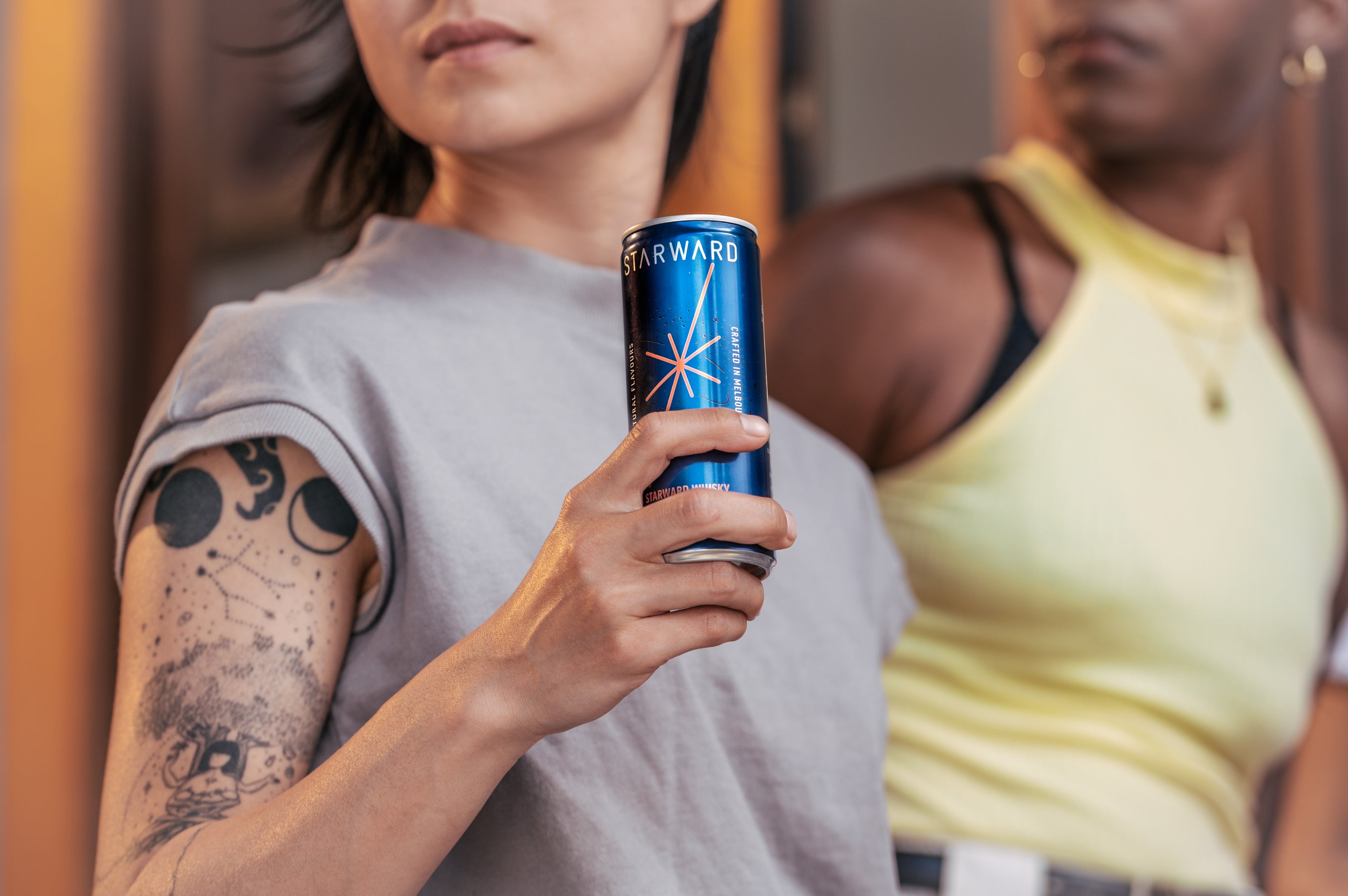 Person with tattoos on arm holding canned cocktail from Starward Whisky