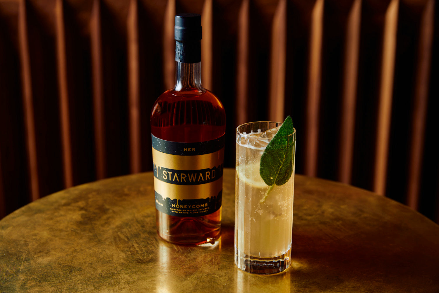 a refrehsing looking lemon coloured cocktail with a bottle of HER Honeycomb whisky at HER Bar in Melbourne