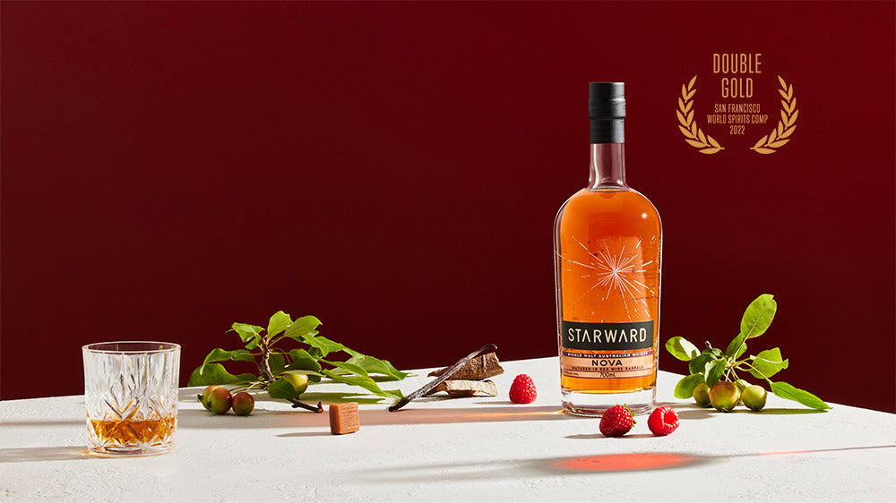 Bottle of Starward Australian Whisky with floral and glass decorations on a deep red background