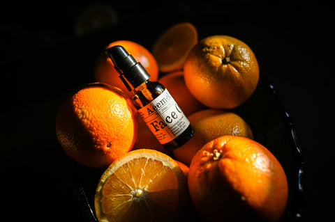 Aeemelia Face Oil, an amber pump top bottle in a pile of brightly colored oranges. 