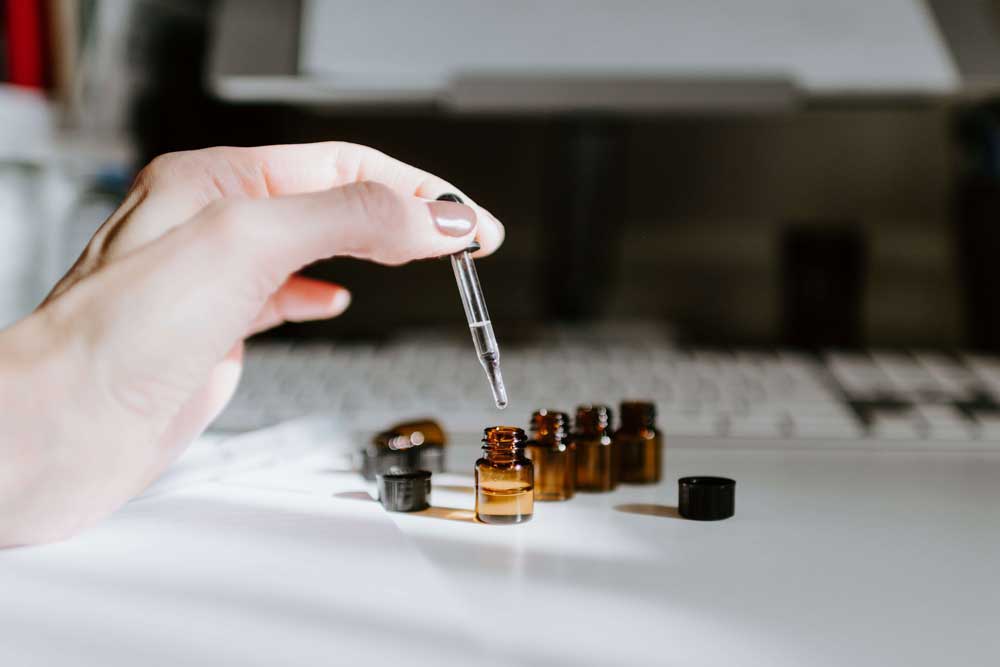 An image of small tincture bottles on a desk with a woman's hand filling the bottles with a liquid presumed to be cannabigerol (CBG).