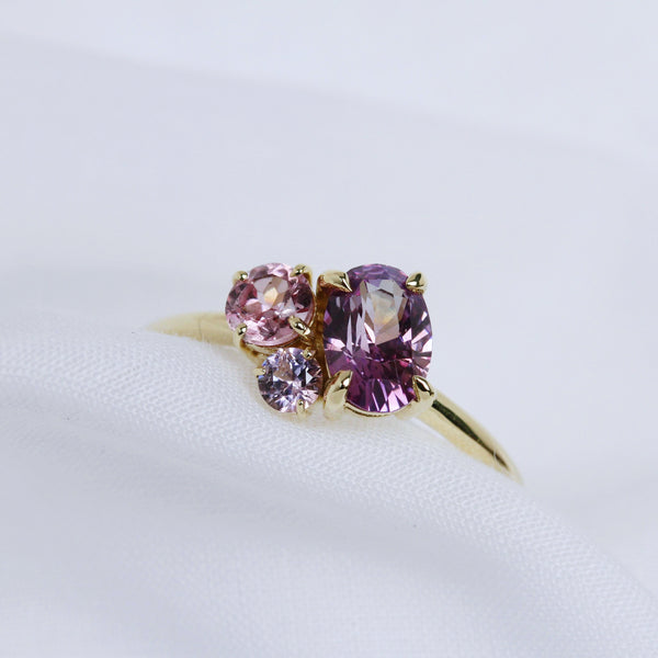 A gold cluster ring of pink and purple sapphires sits on white fabric