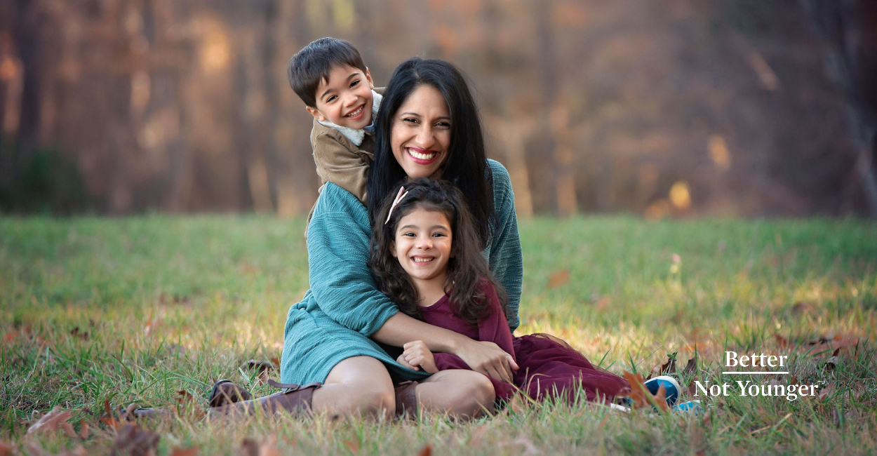 Chami is a 43-year-old mother with two kids, ages 5 and 8. They are at a park playing on the grass and look happy.