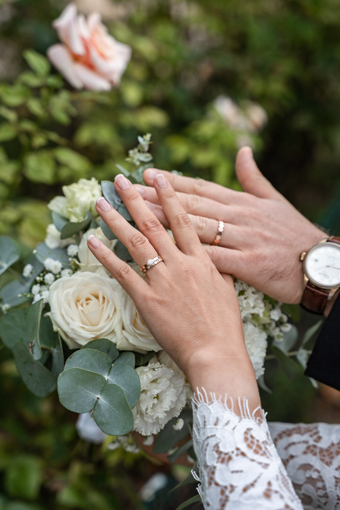 Mains des mariés, ornées de leurs alliances, posées sur un bouquet de roses blanches