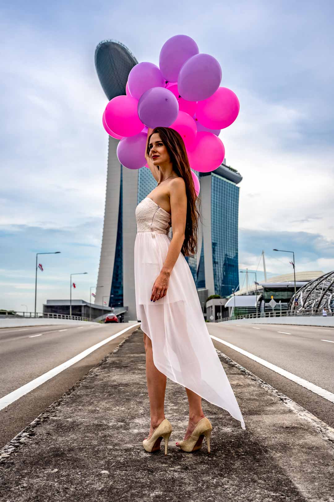 Femme en robe blance posant avec des ballons colorés devant le Marina Bay Sands à Singapour