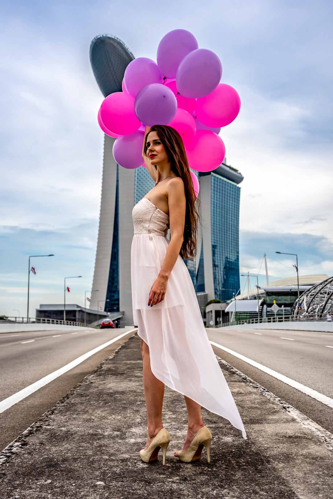 Femme en robe blanche pose avec des ballons colorés devant Marina Bay Sands