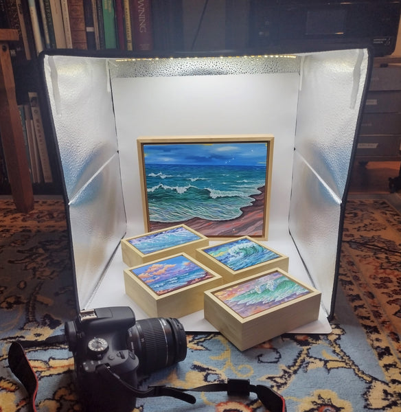 Photo shows five gouache seascapes in floater frames resting in a lightbox next to a DSLR camera.