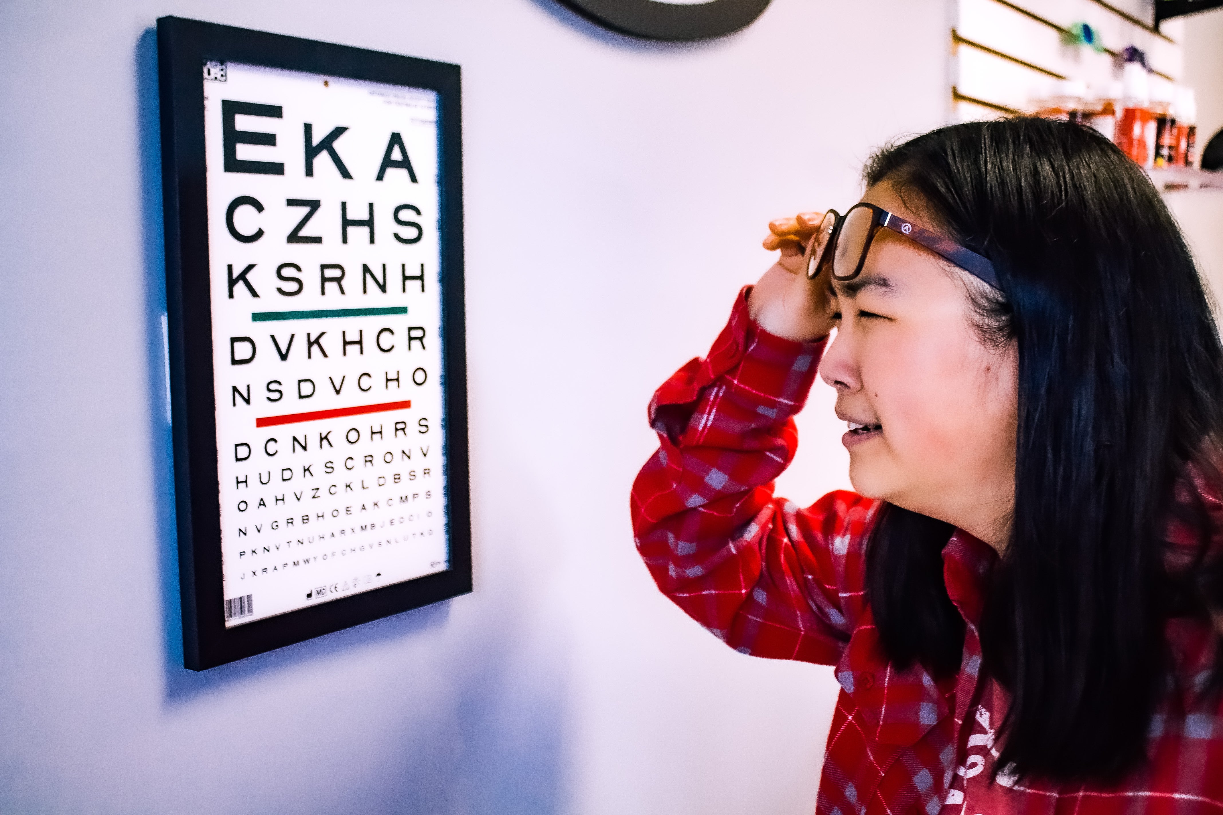 woman squinting at an eye chart on the wall while not wearing her glasses