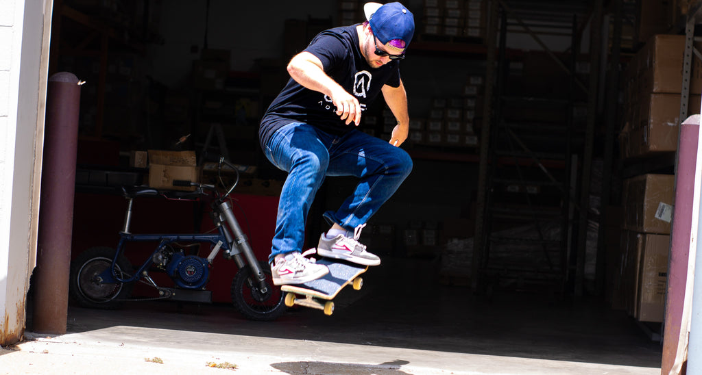 Bizlog wearing a gamer advantage tshirt and glasses doing a jump on a skateboard