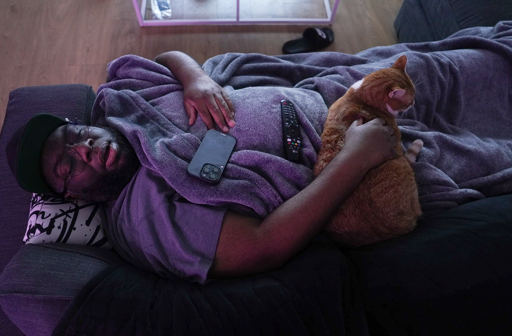 man laying on a bed with his cat asleep with gamer advantage glasses