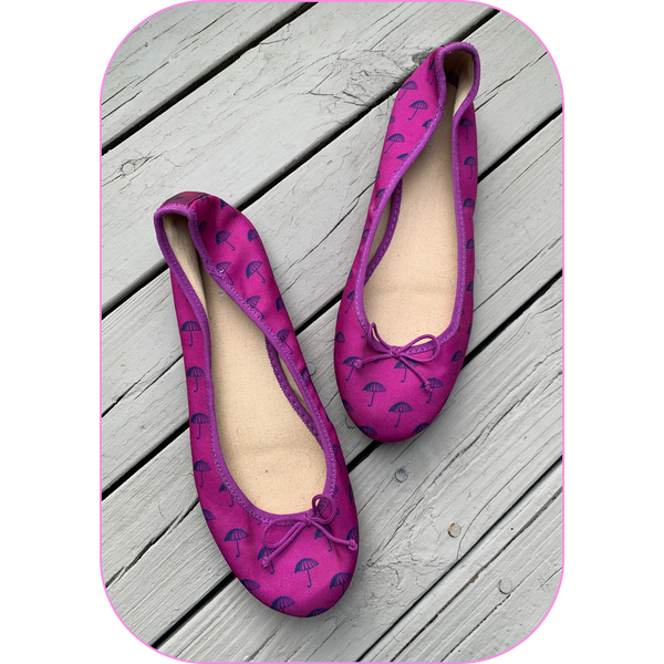 a pair of dark pink slip-on flat shoes with little black umbrellas printed all over them