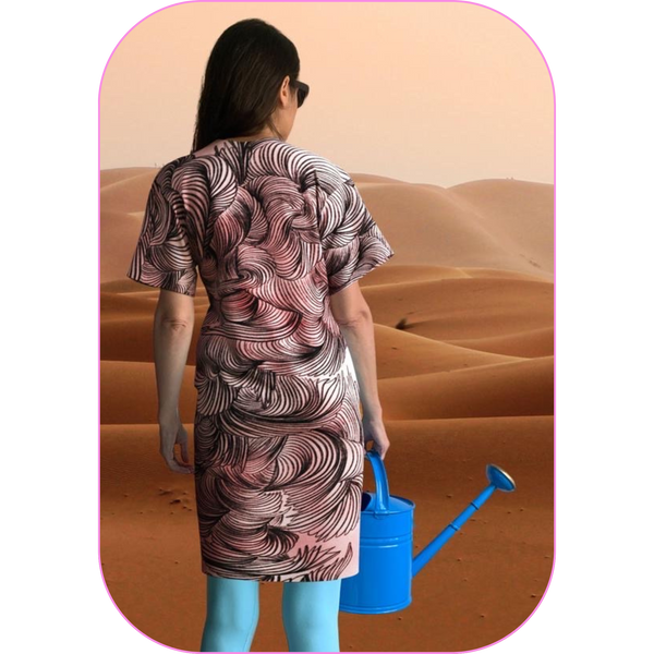 photo of a woman wearing a pink and black digital dress, holding a blue watering can, looking out over an expanse of desert