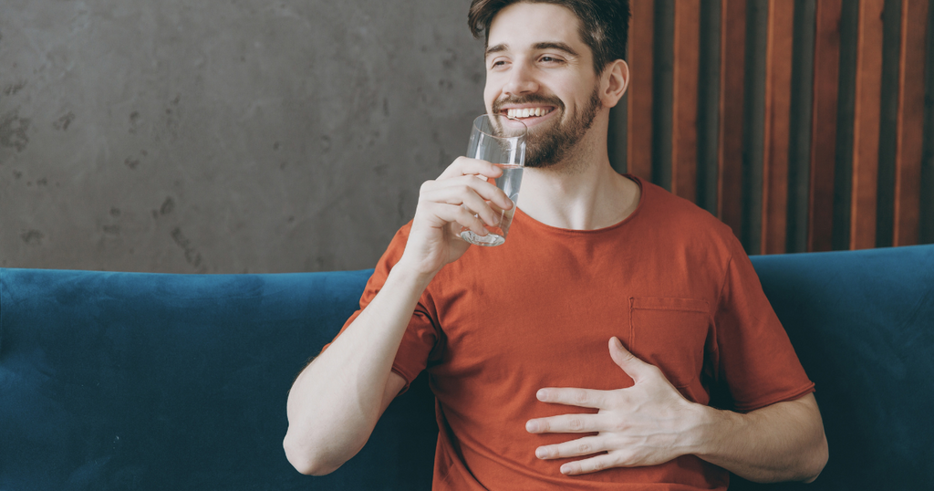 Man drinking water holding his stomach happily